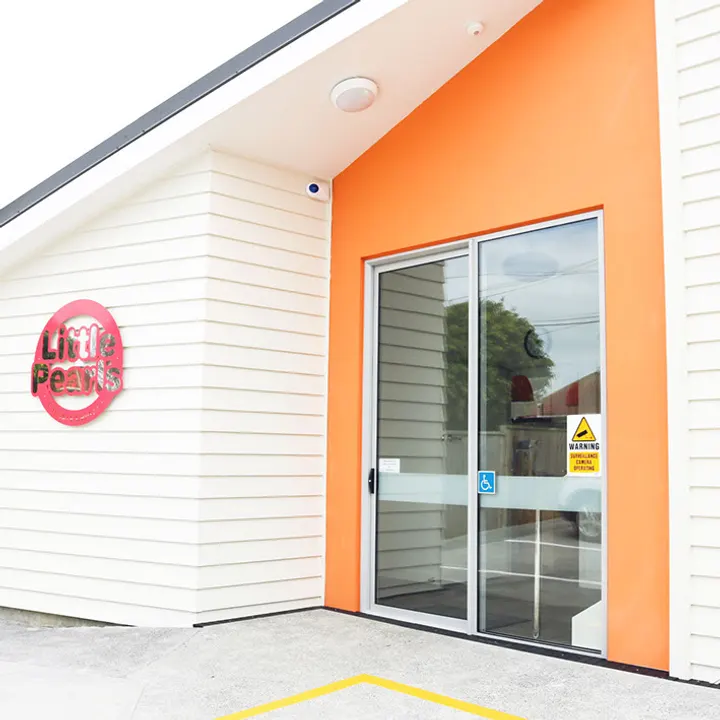 The entrance to a Little Pearls centre: a white and orange building with the Little Pearls logo mounted beside sliding glass doors.
